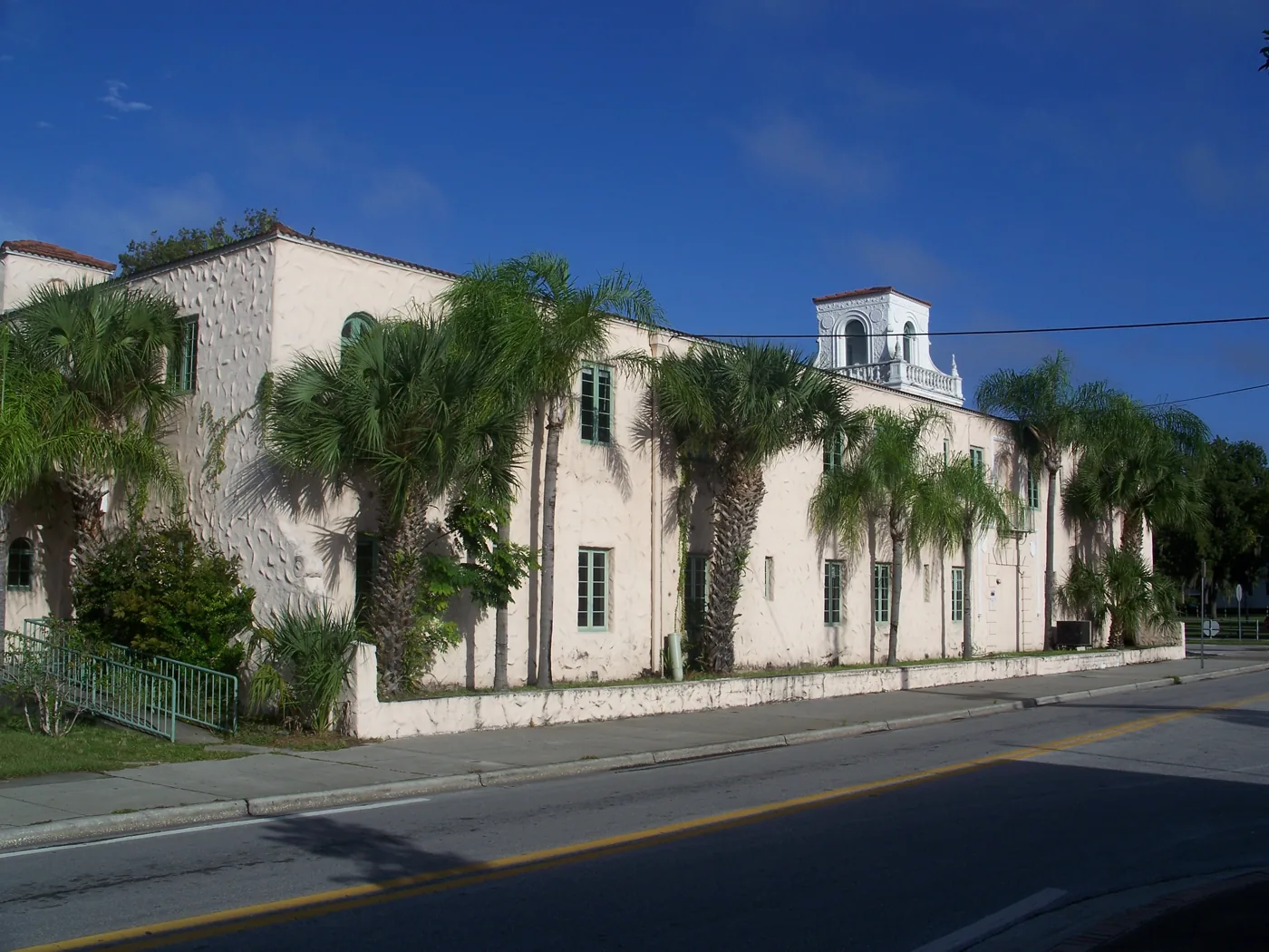 A Spanish-style stucco hotel with arched windows and a red tile roof under palm trees.