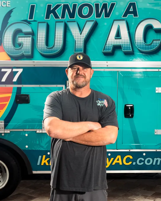 I Know A Guy AC technician standing in front of the branded turquoise truck