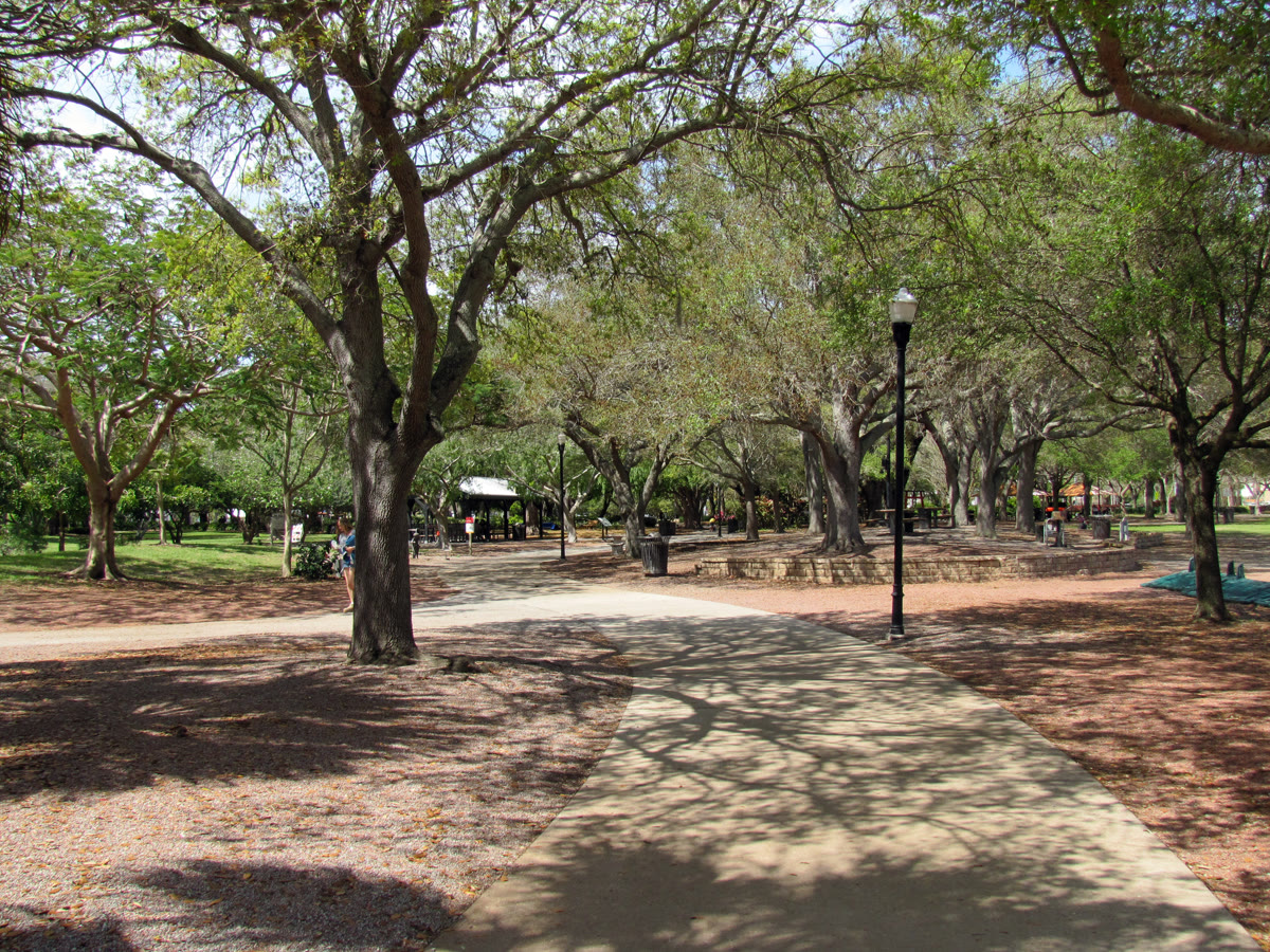 A present-day public park with green lawns, walkways and a lake, apartment buildings visible beyond the trees.